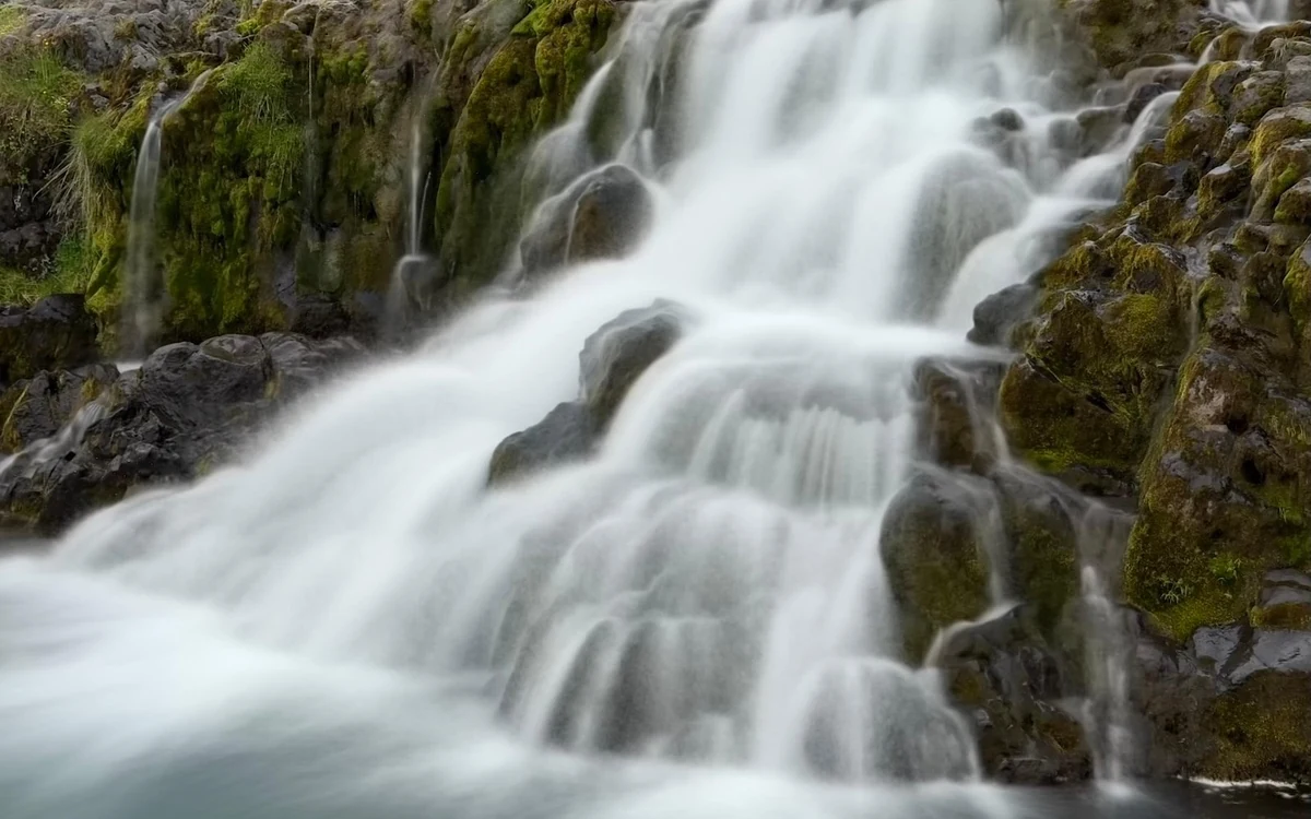 Water spreading over mossy ledges in a tiered fall in the Westfjords