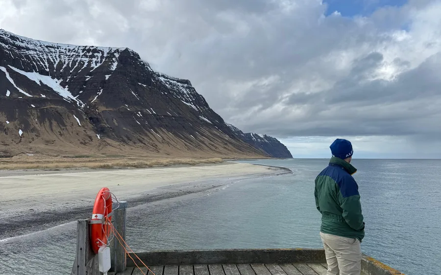 A person on the pier looking out to the snow-streaked mountains